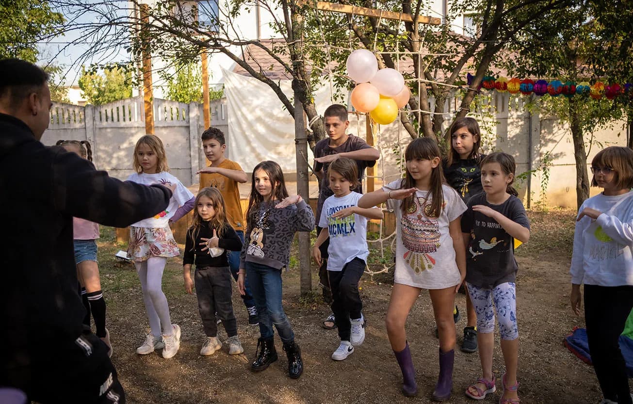 Copii dansează cu animatorul la o petrecere în curtea La Căprițe, sub baloane și ghirlande