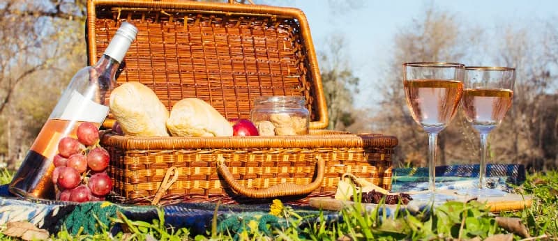 Coș de picnic cu pâine, struguri și două pahare de vin, pe iarbă